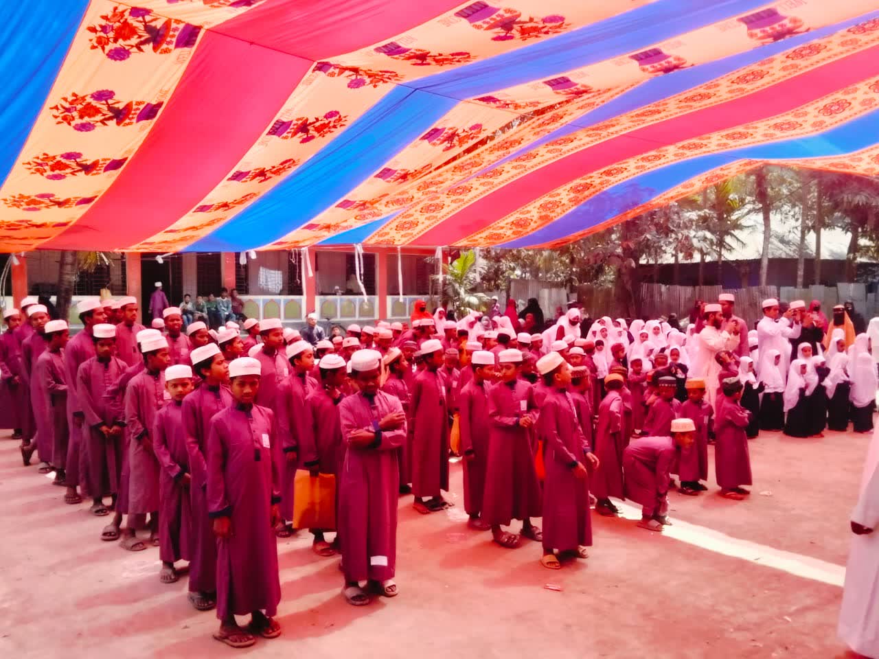 Rows of boys in maroon uniforms standing under a colorful tent